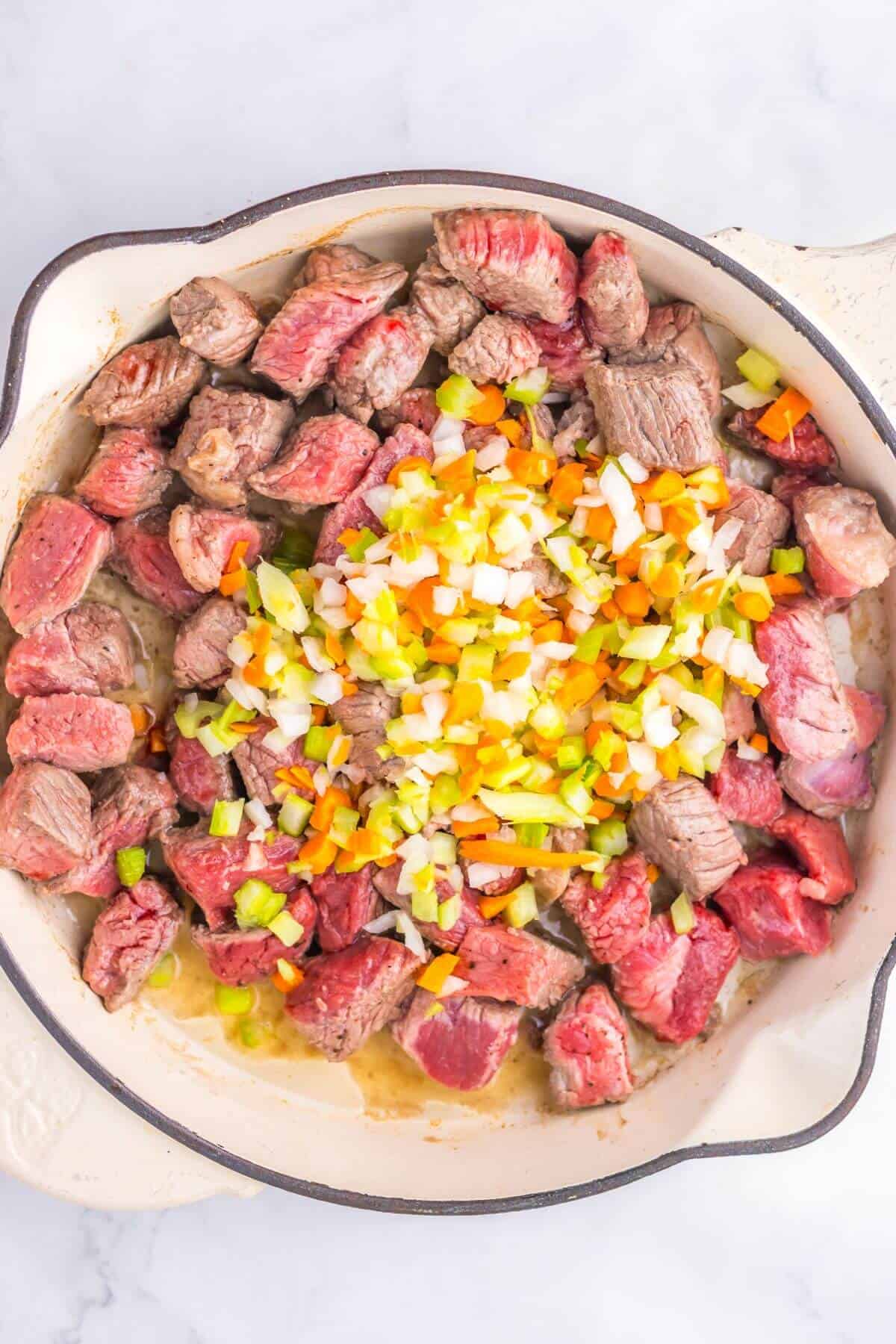 Chunks of beef and diced vegetables in a cast iron skillet, ready for cooking.
