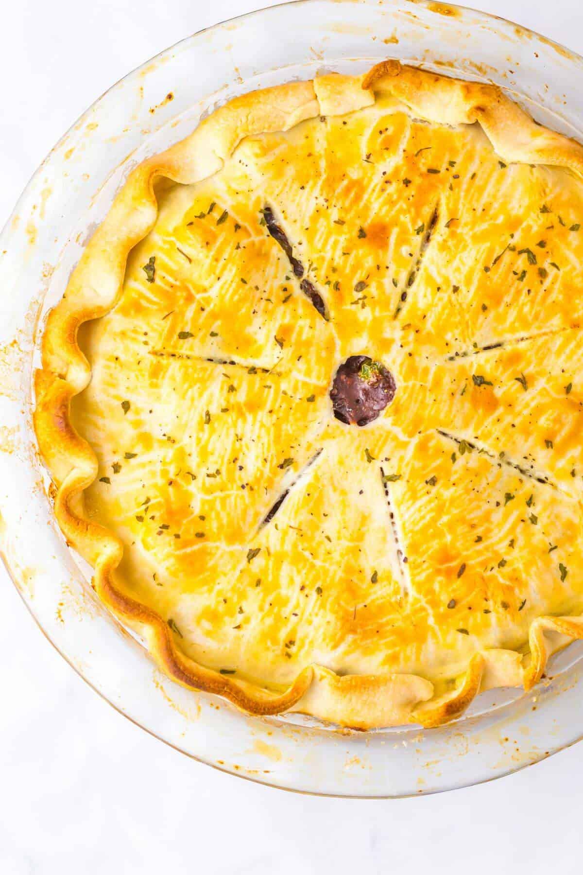 A golden-brown pie with a ruffled crust and a small circular opening at the center, placed on a glass pie dish.