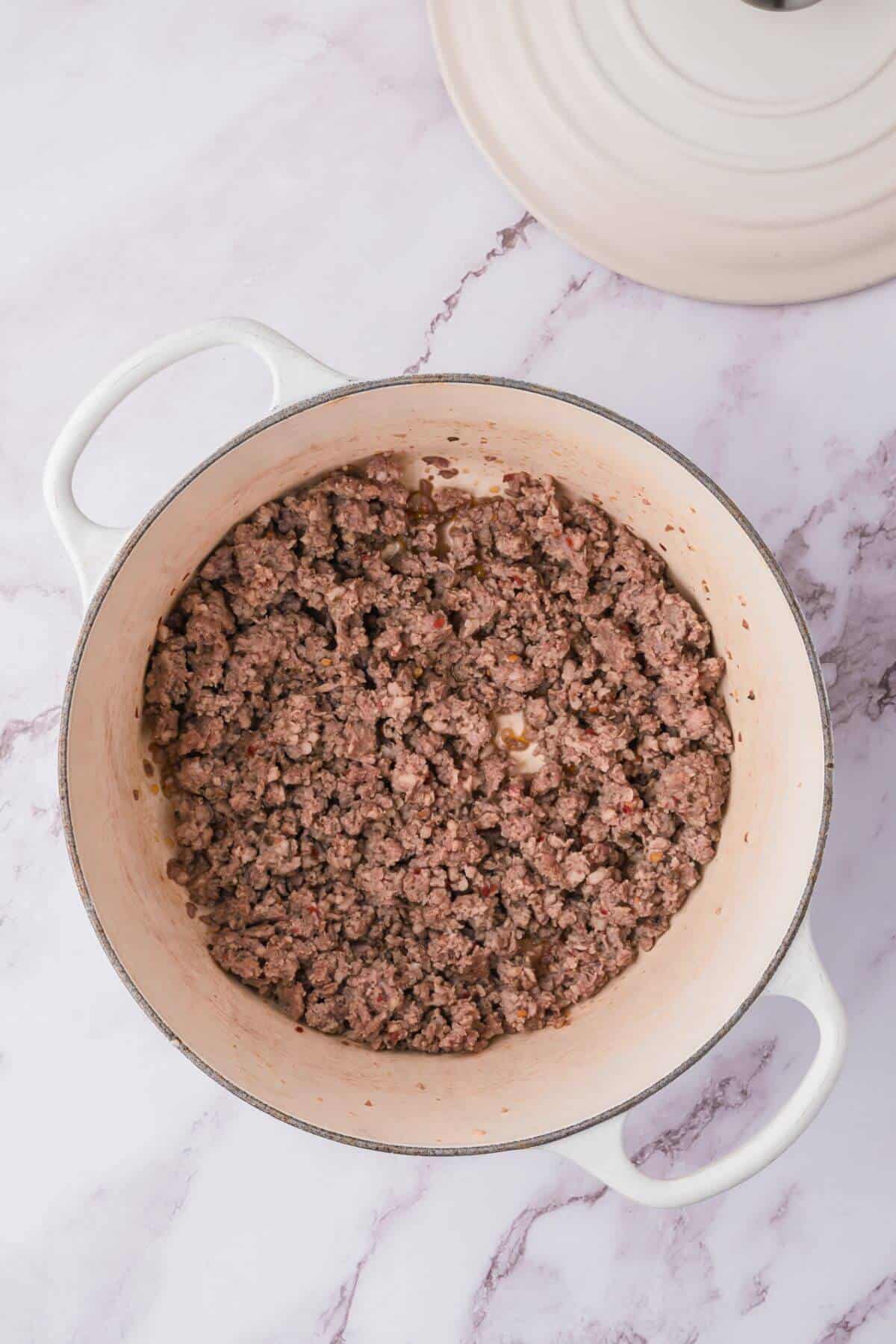 Ground beef cooking in a white pot on a marble countertop.