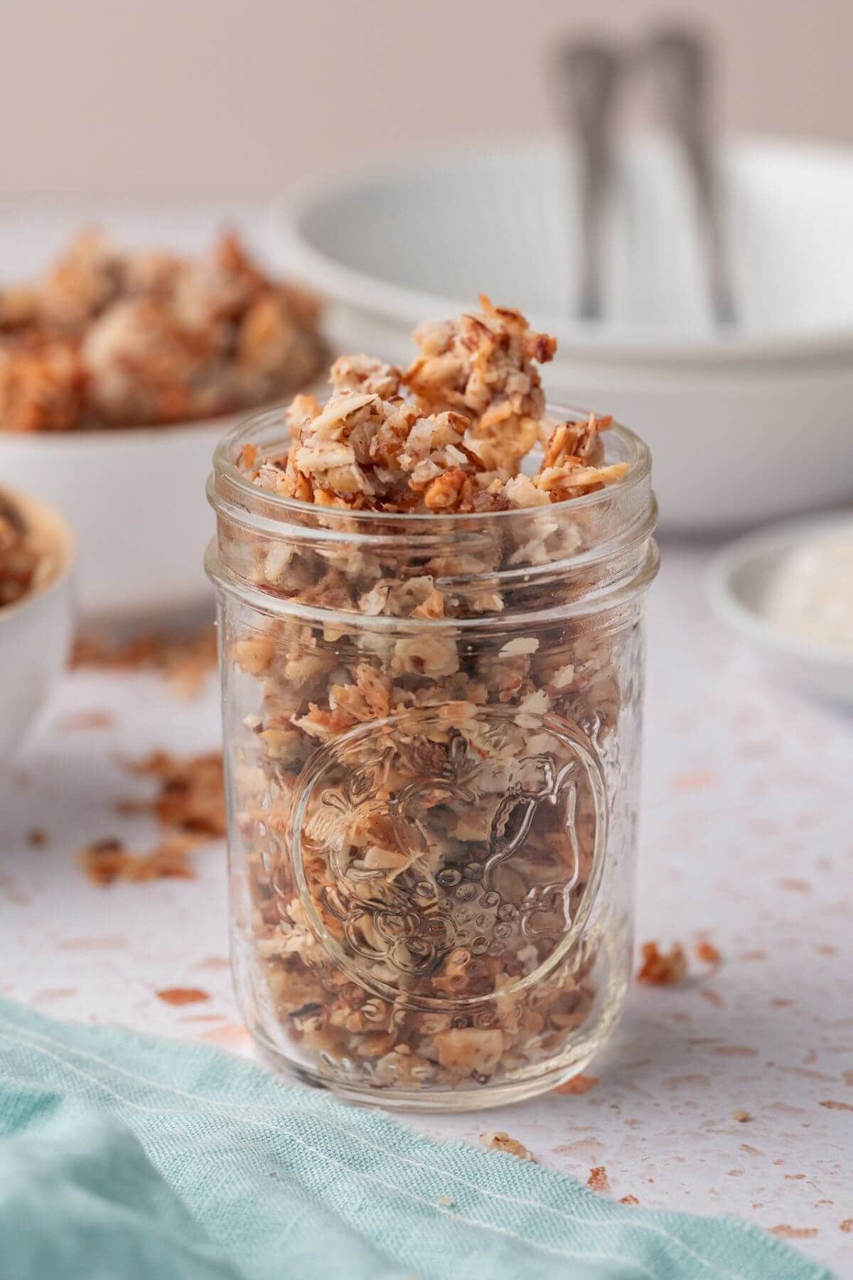 A jar filled with homemade granola, surrounded by scattered granola pieces on a table.
