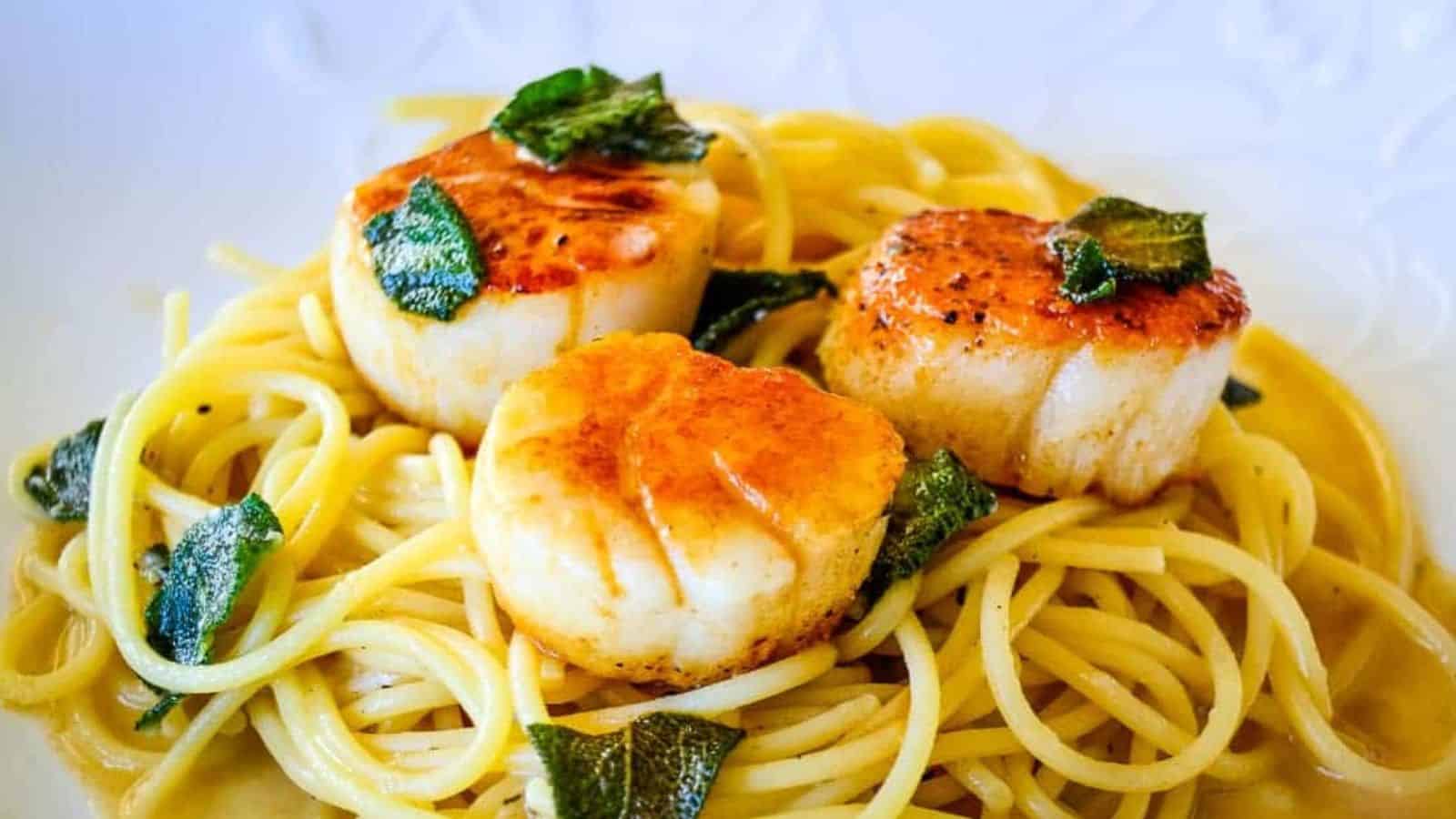 A serving of pasta topped with a seared scallops and a sage brown butter sauce.