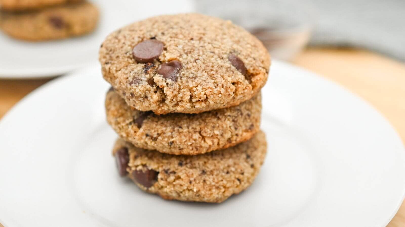 Three stacked chocolate chip cookies on a white plate.