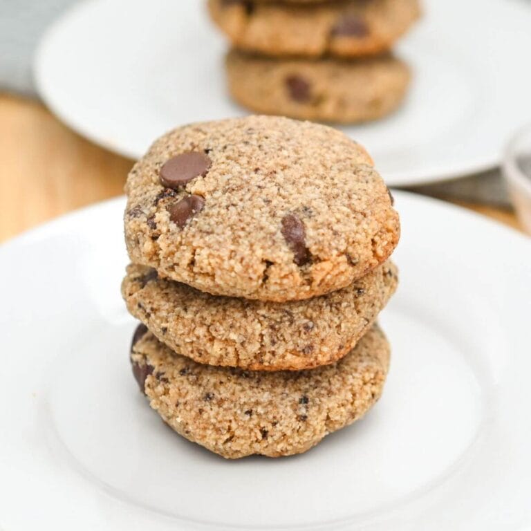 Three stacked chocolate chip cookies on a white plate.