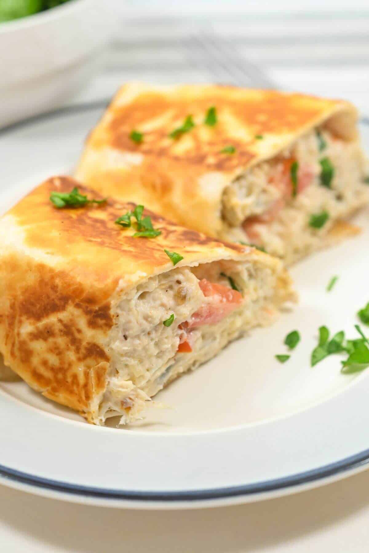Two slices of a grilled wrap on a white plate, filled with a creamy mixture and garnished with fresh parsley.