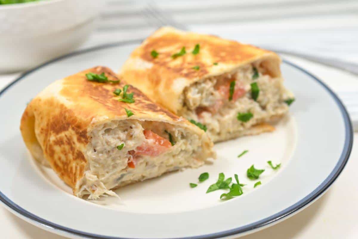 Two grilled wraps stuffed with a creamy chicken filling, garnished with parsley, are served on a white plate.