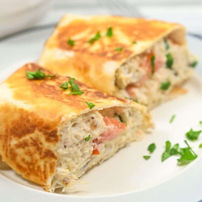 Two halves of a toasted wrap filled with tuna, tomatoes, and herbs, garnished with chopped parsley, on a white plate.