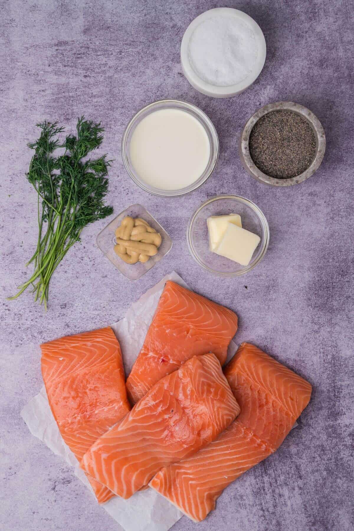 Raw salmon fillets, fresh herbs, cream, sugar, mustard, butter, and pepper arranged on a textured surface.