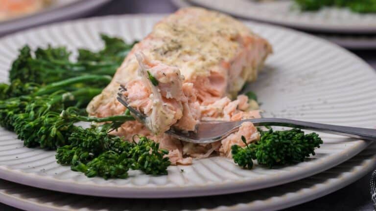A plated piece of seasoned salmon with a portion removed on a fork, served alongside steamed broccolini.