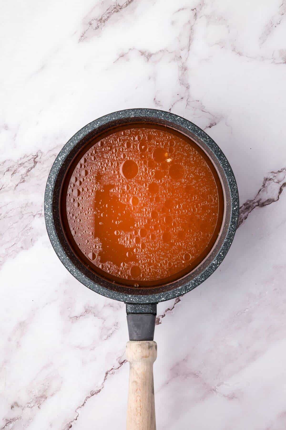 A pot filled with bubbling red liquid with oil droplets, set on a marbled white surface.