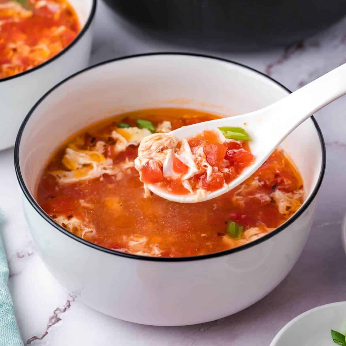 A bowl of tomato and egg drop soup with a spoon lifting a portion.
