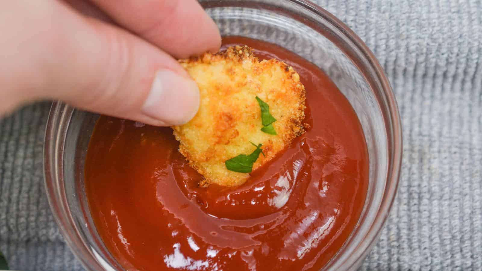 Hand dipping a breaded nugget into a bowl of ketchup.