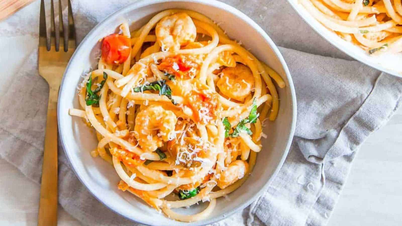 Bucatini pasta with shrimp in a white bowl.