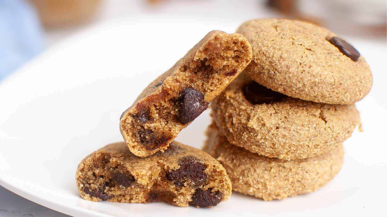 A stack of four chocolate chip cookies, with one broken in half, placed on a white plate.