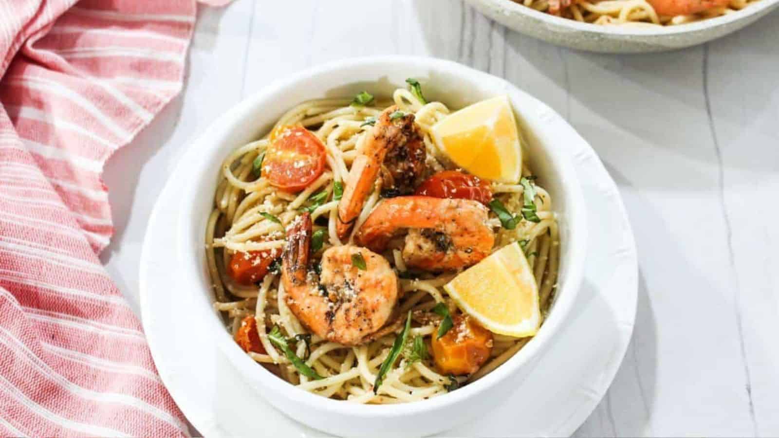 A bowl of pasta with shrimp and tomatoes.