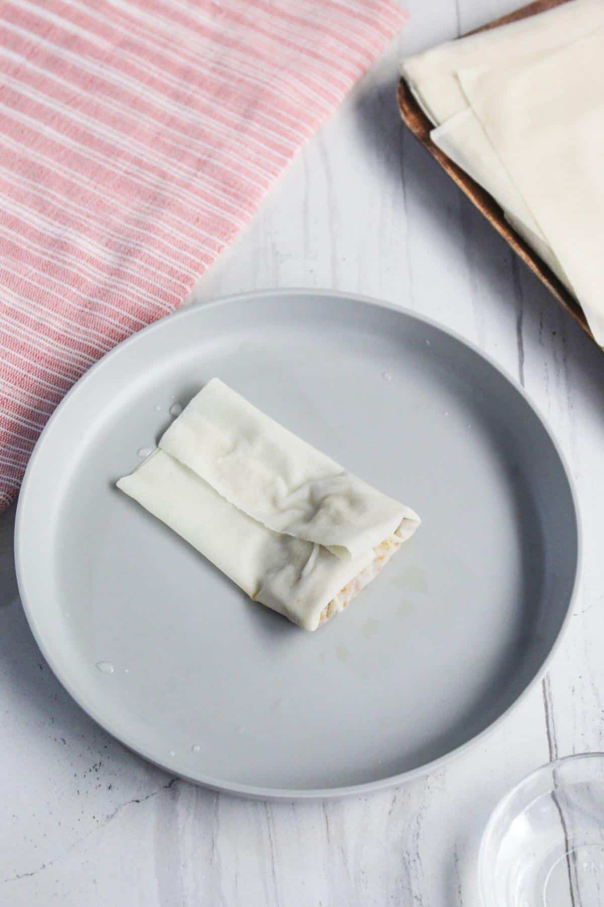 A single folded pastry on a gray plate with a striped pink cloth and pastry sheets in the background.