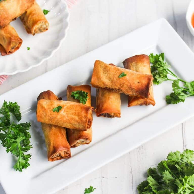 Fried spring rolls on a rectangular white plate, garnished with parsley.