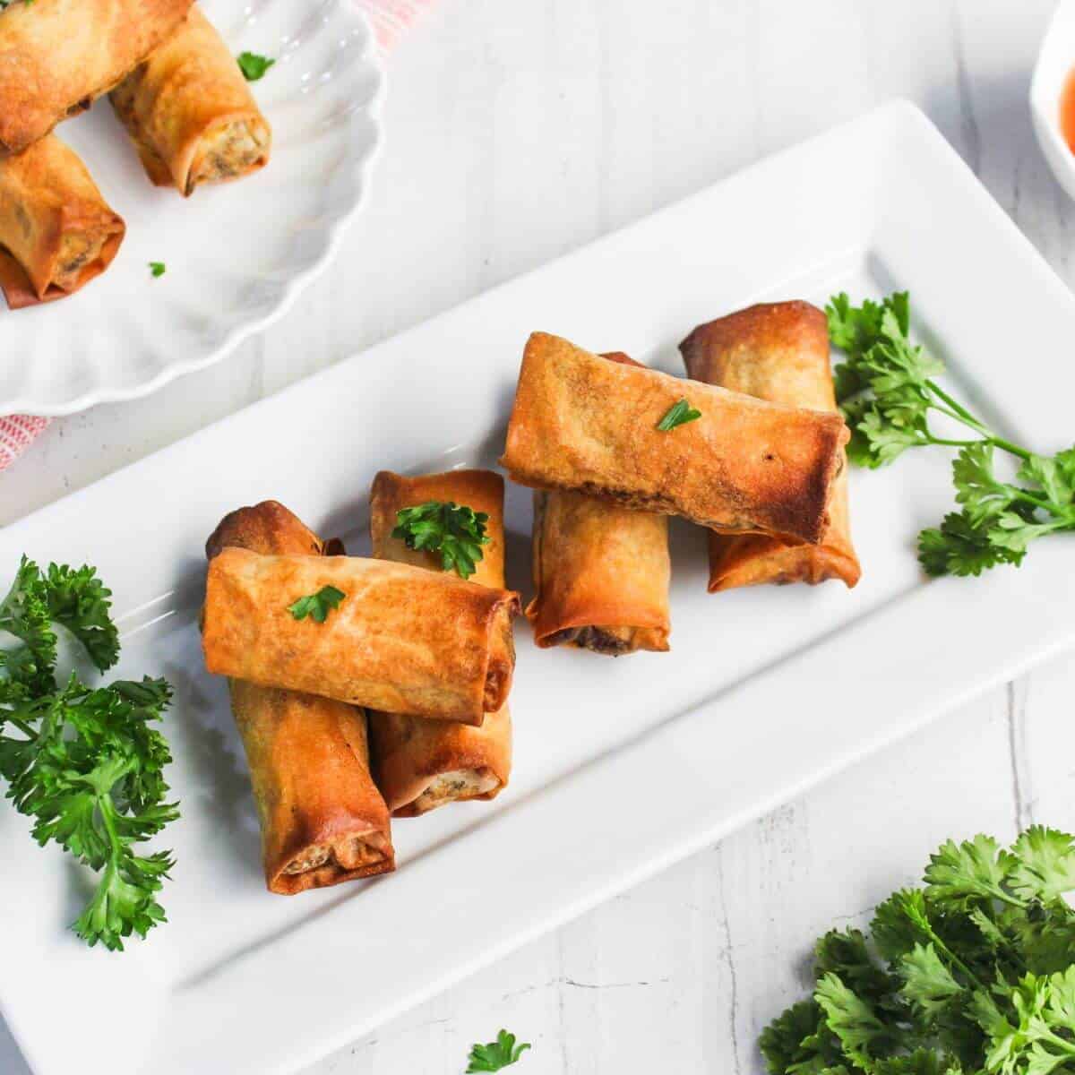 Fried spring rolls on a rectangular white plate, garnished with parsley.