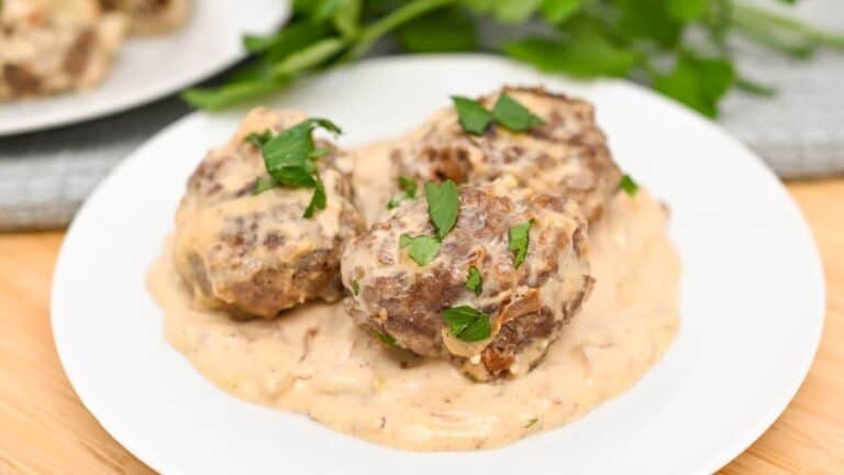 Three meatballs with creamy sauce on a white plate, garnished with green herbs.