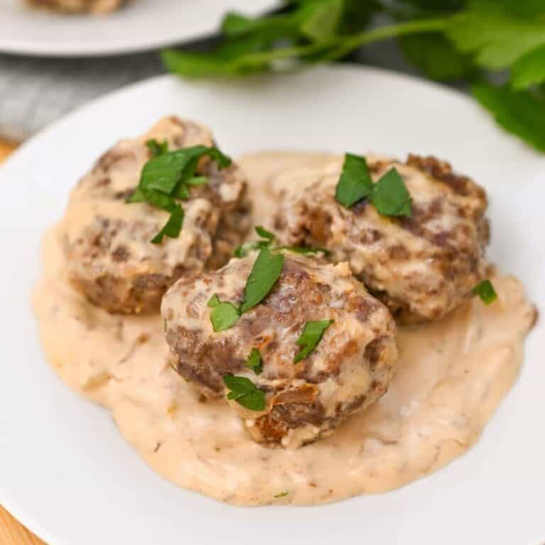 Three meatballs covered in creamy sauce on a white plate, garnished with chopped parsley.