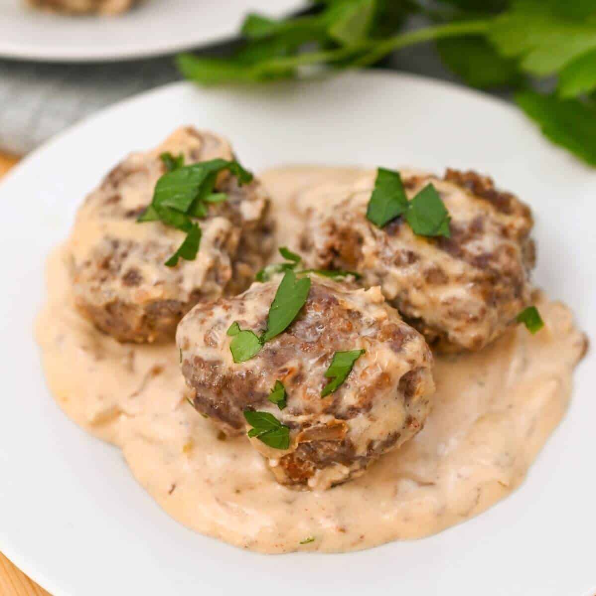 Three meatballs covered in creamy sauce on a white plate, garnished with chopped parsley.