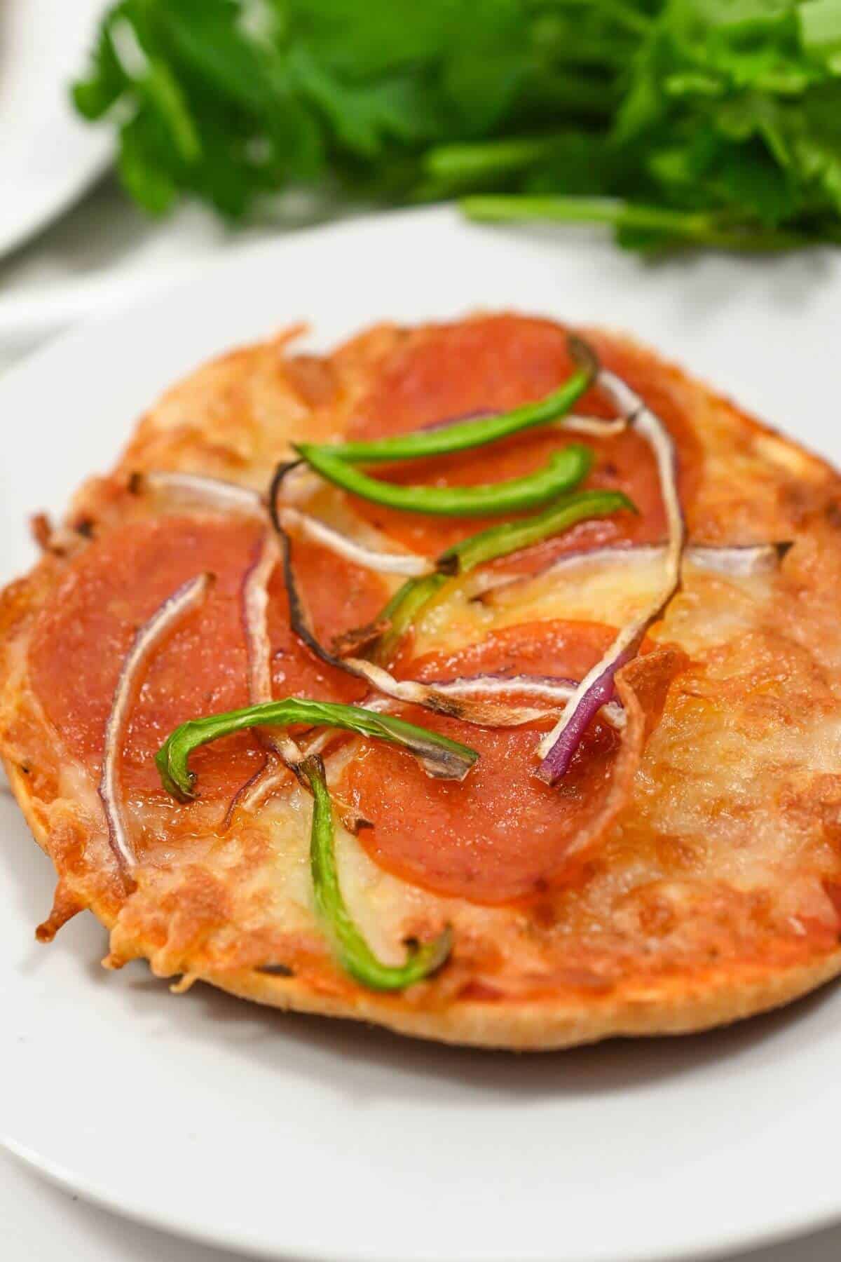 A small pizza with pepperoni, green peppers, and red onions on a white plate.