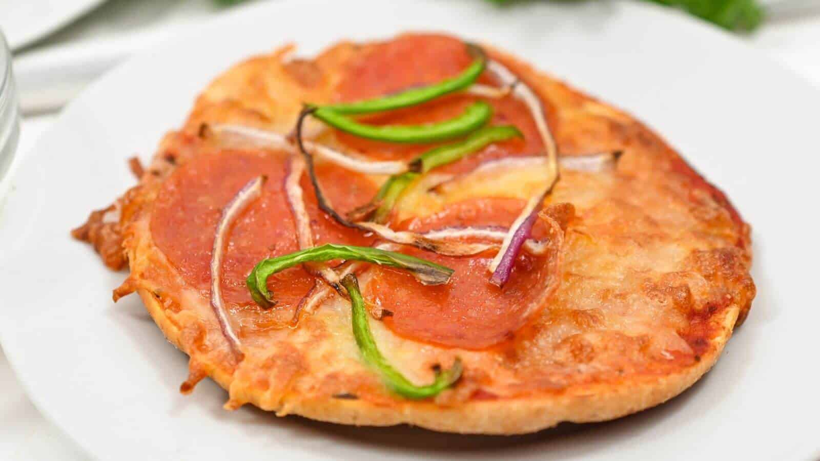 A small pizza with pepperoni, green peppers, and onion slices on a white plate.