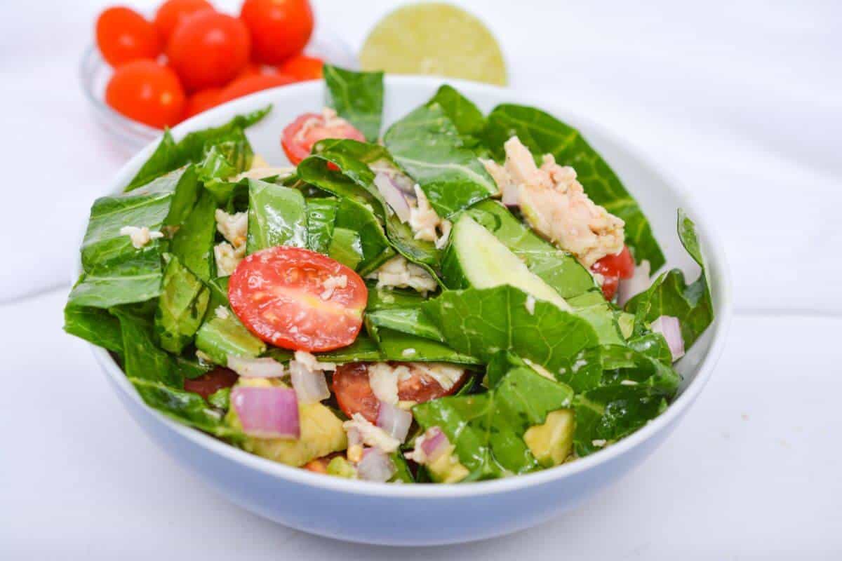 A bowl of salad with lettuce, cherry tomatoes, cucumber, red onion, and chicken. A halved lime and a bowl of cherry tomatoes are in the background.