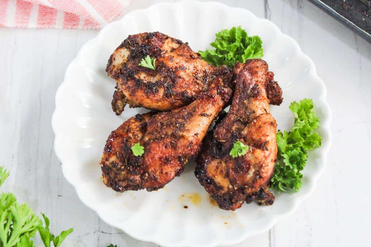 Three pieces of seasoned, cooked chicken drumsticks served on a white plate with sprigs of parsley for garnish.