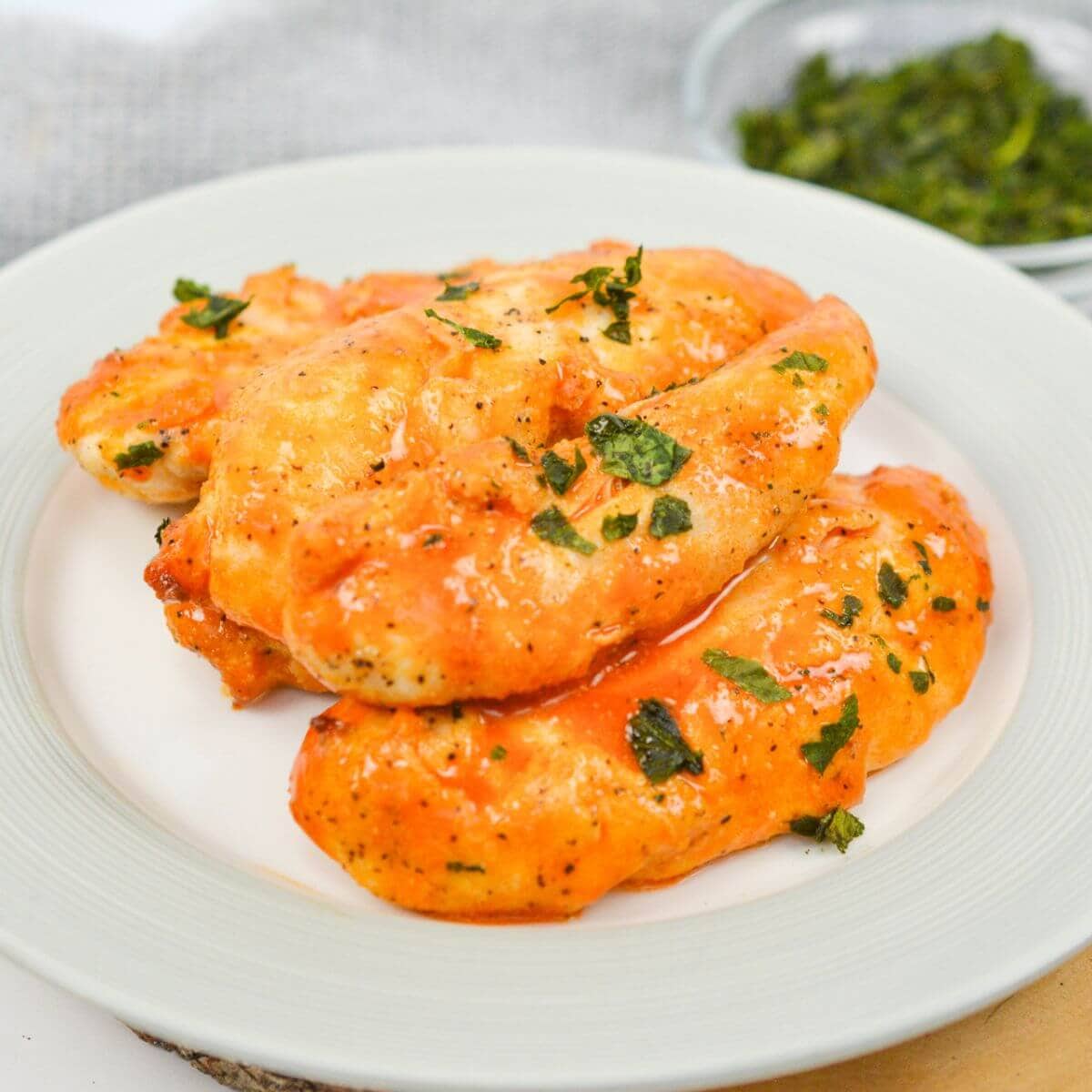 Plate of glazed chicken fillets garnished with herbs, on a white plate.