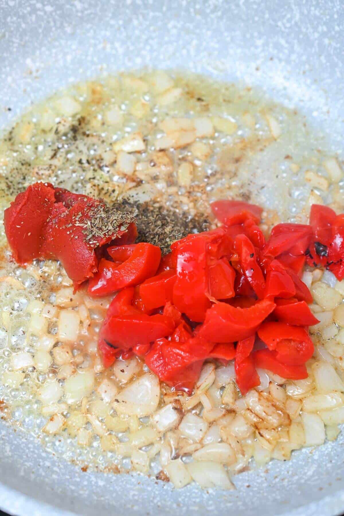 Chopped red peppers and onions sautéing in a pan with spices and oil.