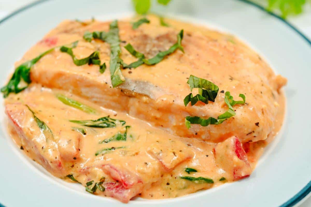 Creamy tomato basil chicken breast on a white plate, garnished with chopped basil.