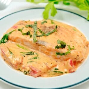 A plate of chicken breast with creamy tomato sauce, spinach, and herbs, garnished with chopped basil.