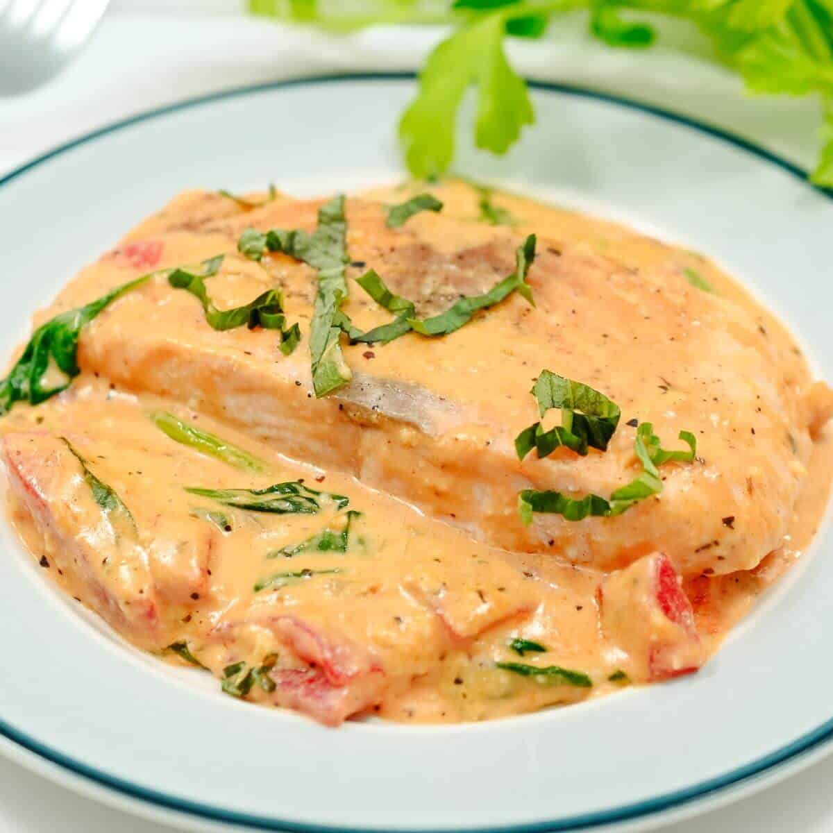 A plate of chicken breast with creamy tomato sauce, spinach, and herbs, garnished with chopped basil.