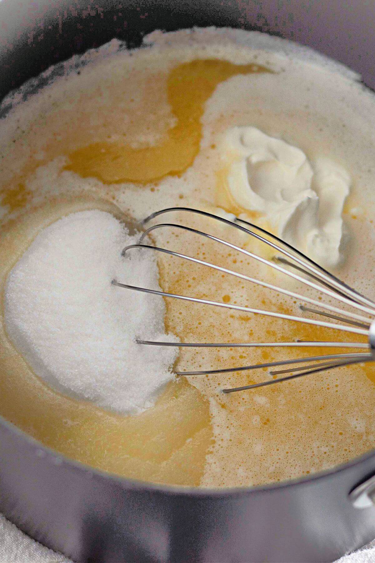 Whisk in a pot mixing sugar, butter, and cream, creating a light, frothy mixture.