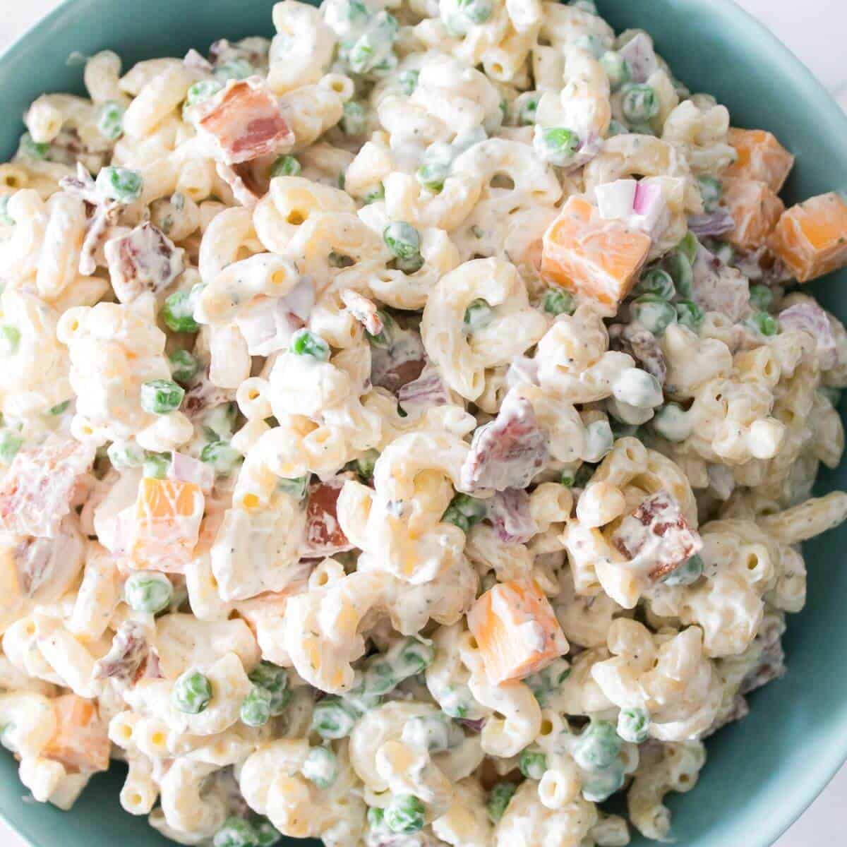 A bowl of macaroni salad with peas, diced cheddar cheese, red onions, and a creamy dressing.