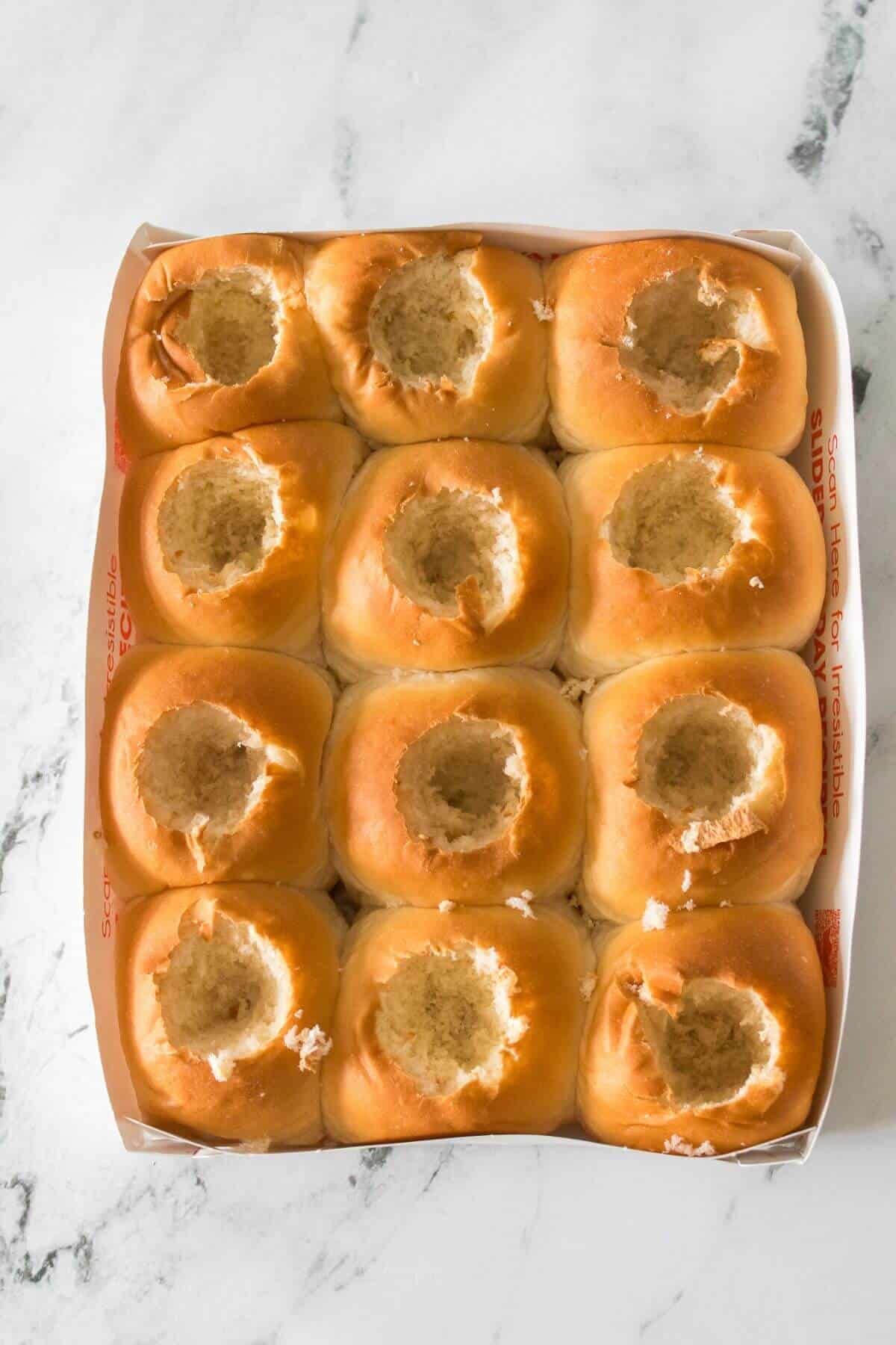 A tray of twelve bread rolls arranged in a 3x4 grid, each with a hole scooped out from the top center.