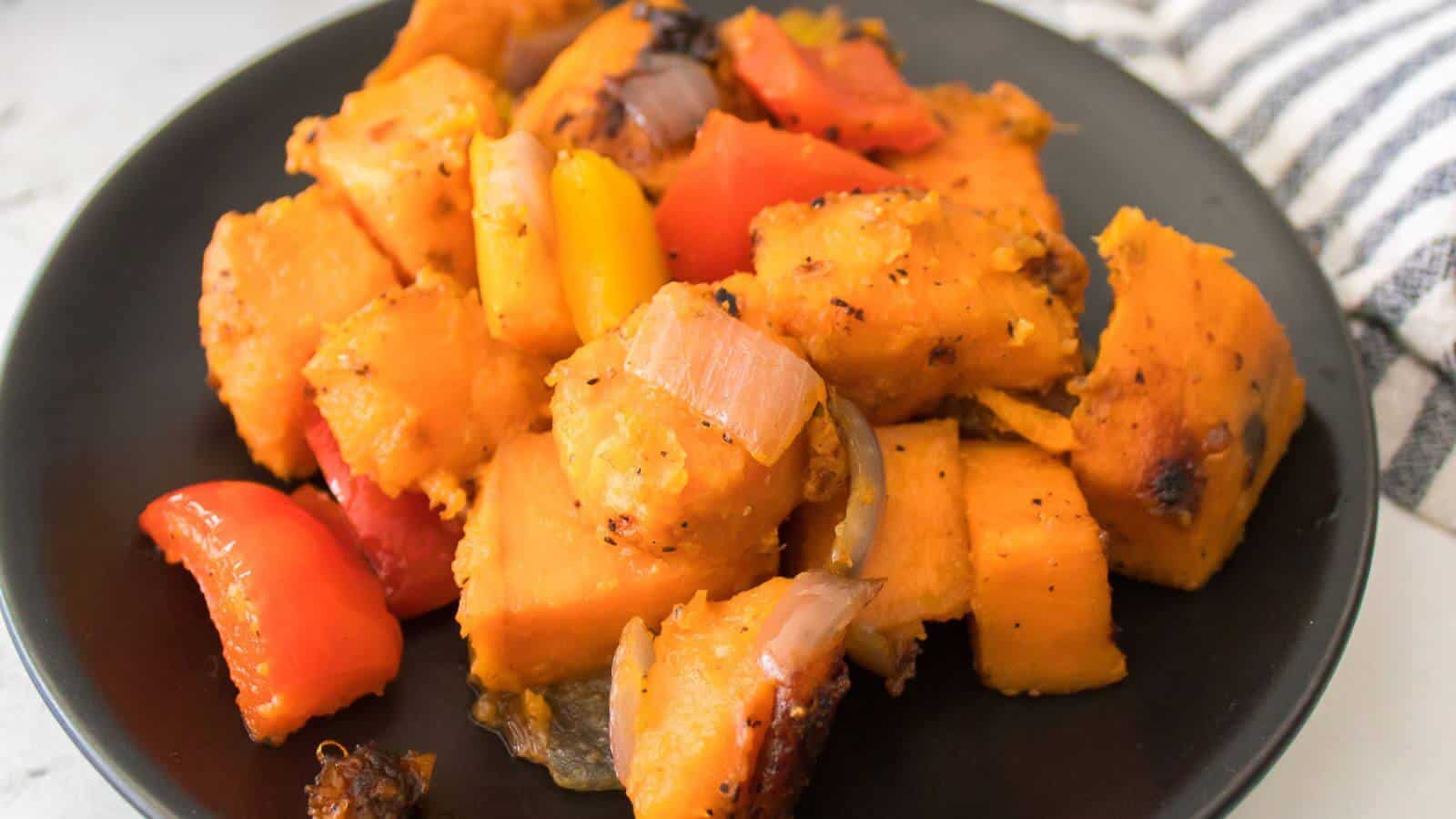 A black plate filled with roasted sweet potato cubes, red and yellow bell peppers, and onion pieces.