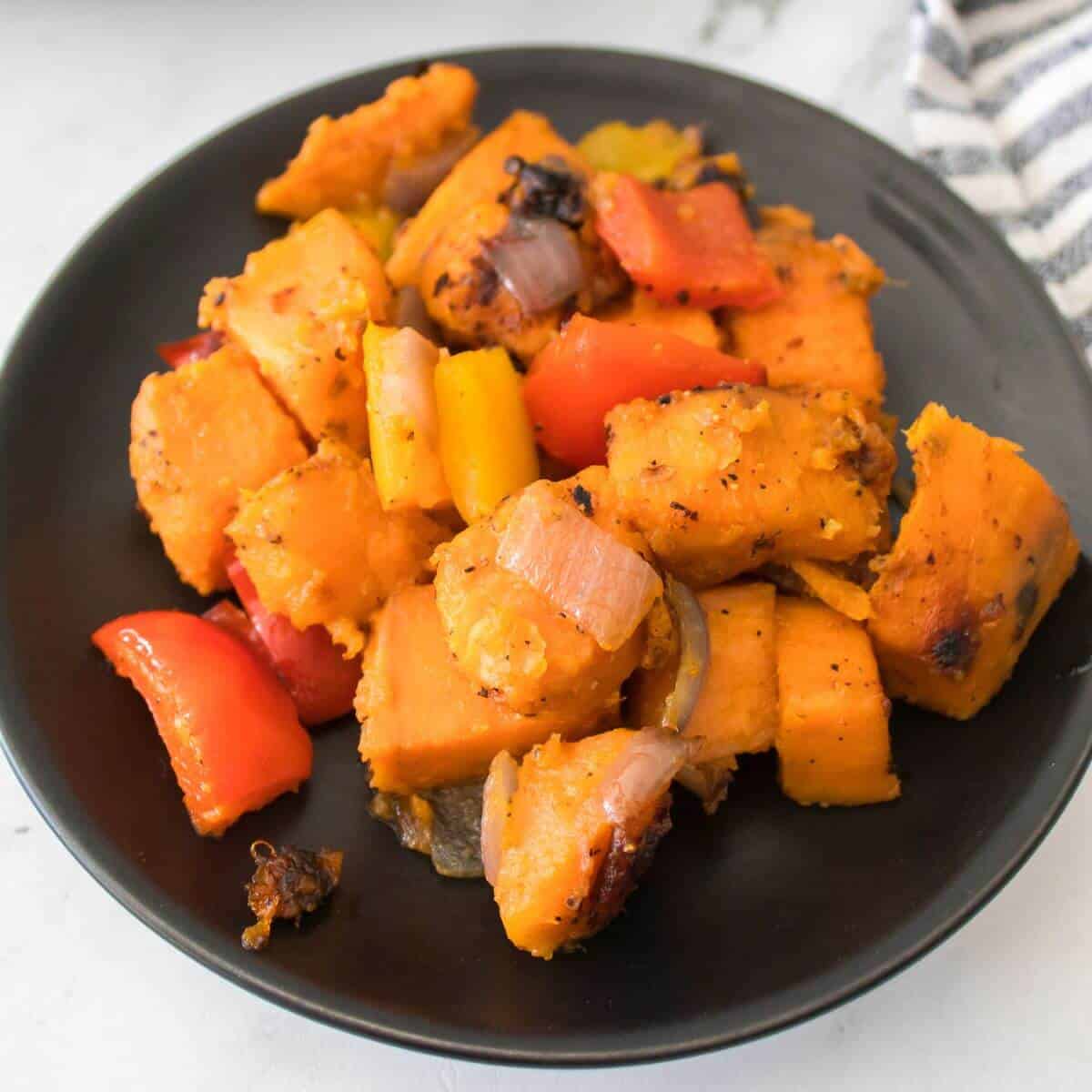 A black plate with roasted sweet potato chunks, red and yellow bell peppers, and pieces of onion.