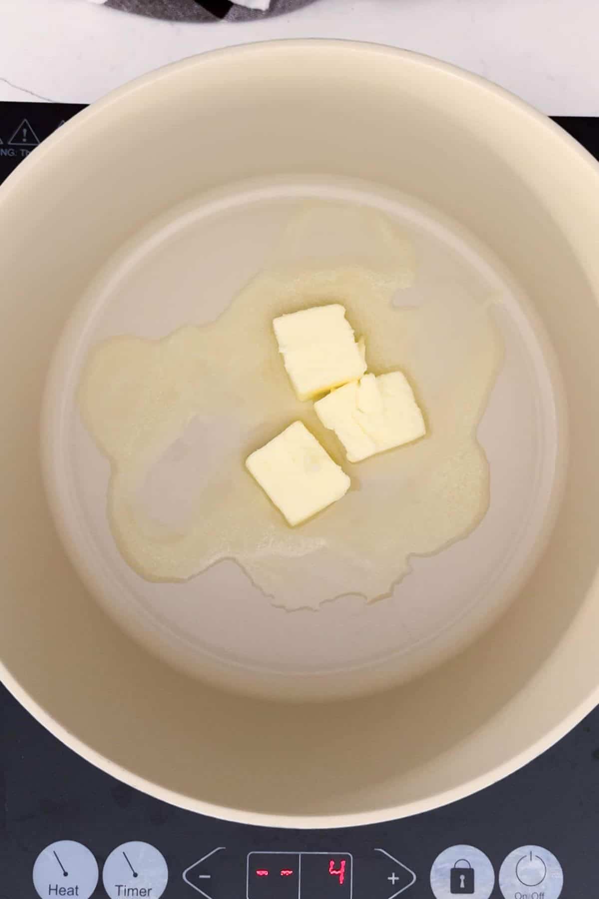Three cubes of butter melting in a beige pot on an induction cooktop set to heat level 4.