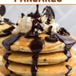 A stack of pancakes topped with chocolate sauce, whipped cream, and Oreo cookie pieces, with "OREO PANCAKES" written above.