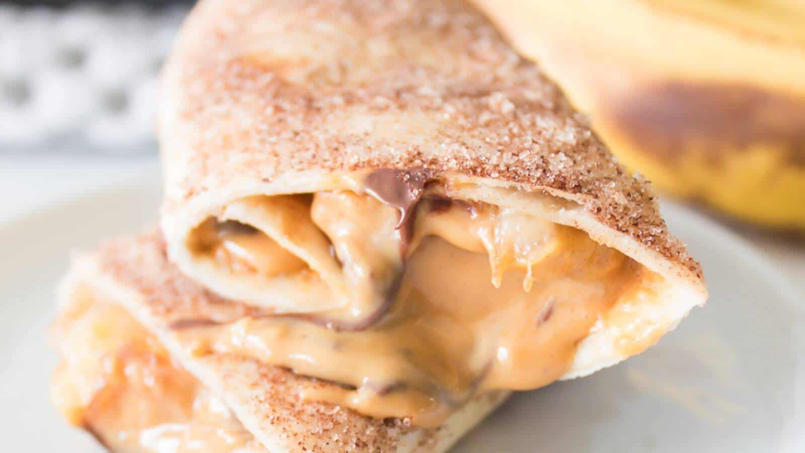 Close-up of two tortilla wraps filled with melted peanut butter and chocolate, stacked on a plate, with a banana in the background.