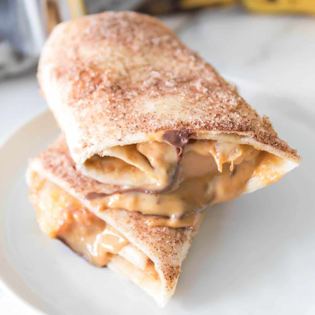 Two cinnamon-sugar coated pastry wraps filled with melted peanut butter and chocolate, stacked on a white plate.