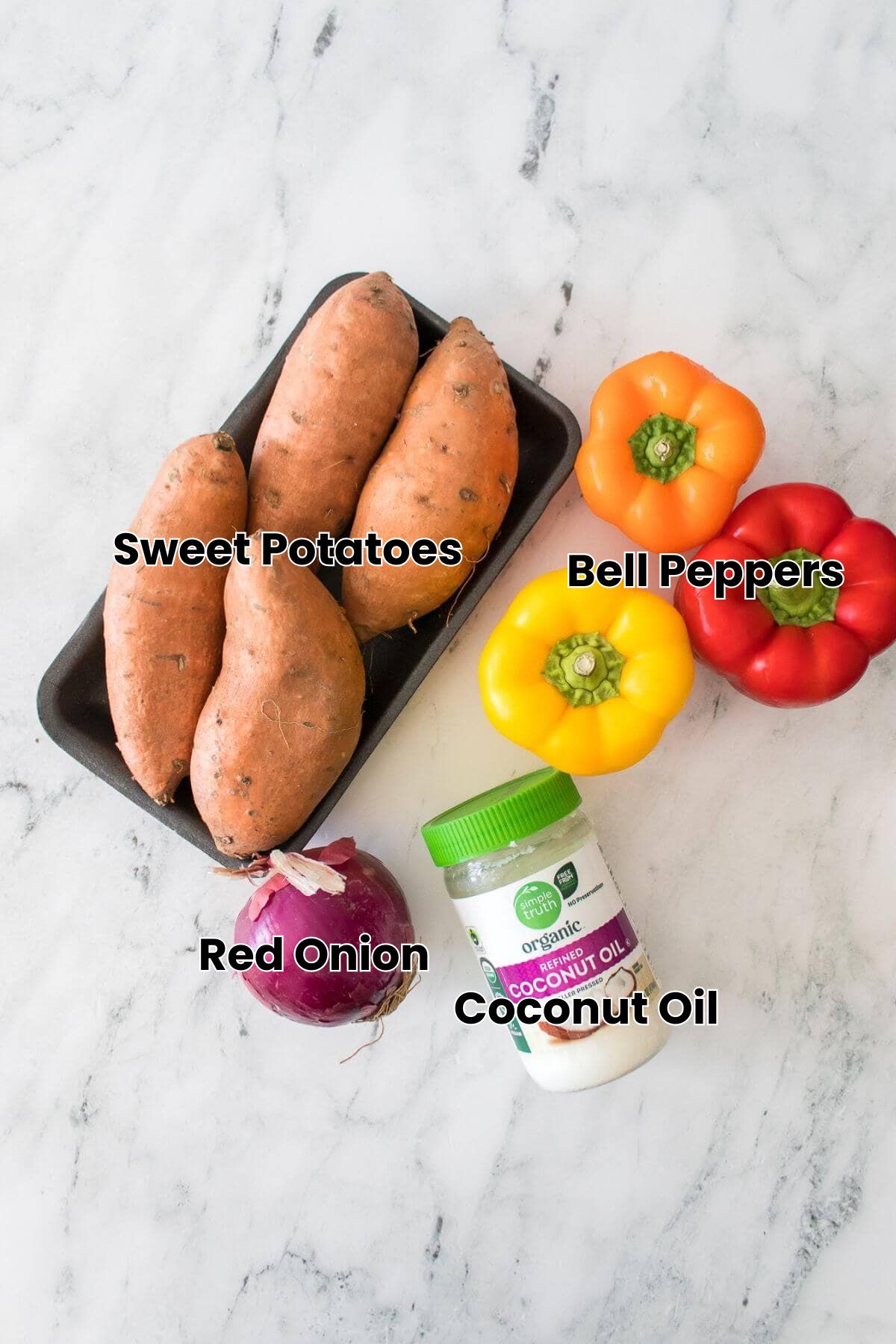 A tray of sweet potatoes, a red onion, three bell peppers (orange, yellow, red), and a jar of coconut oil on a marble surface.