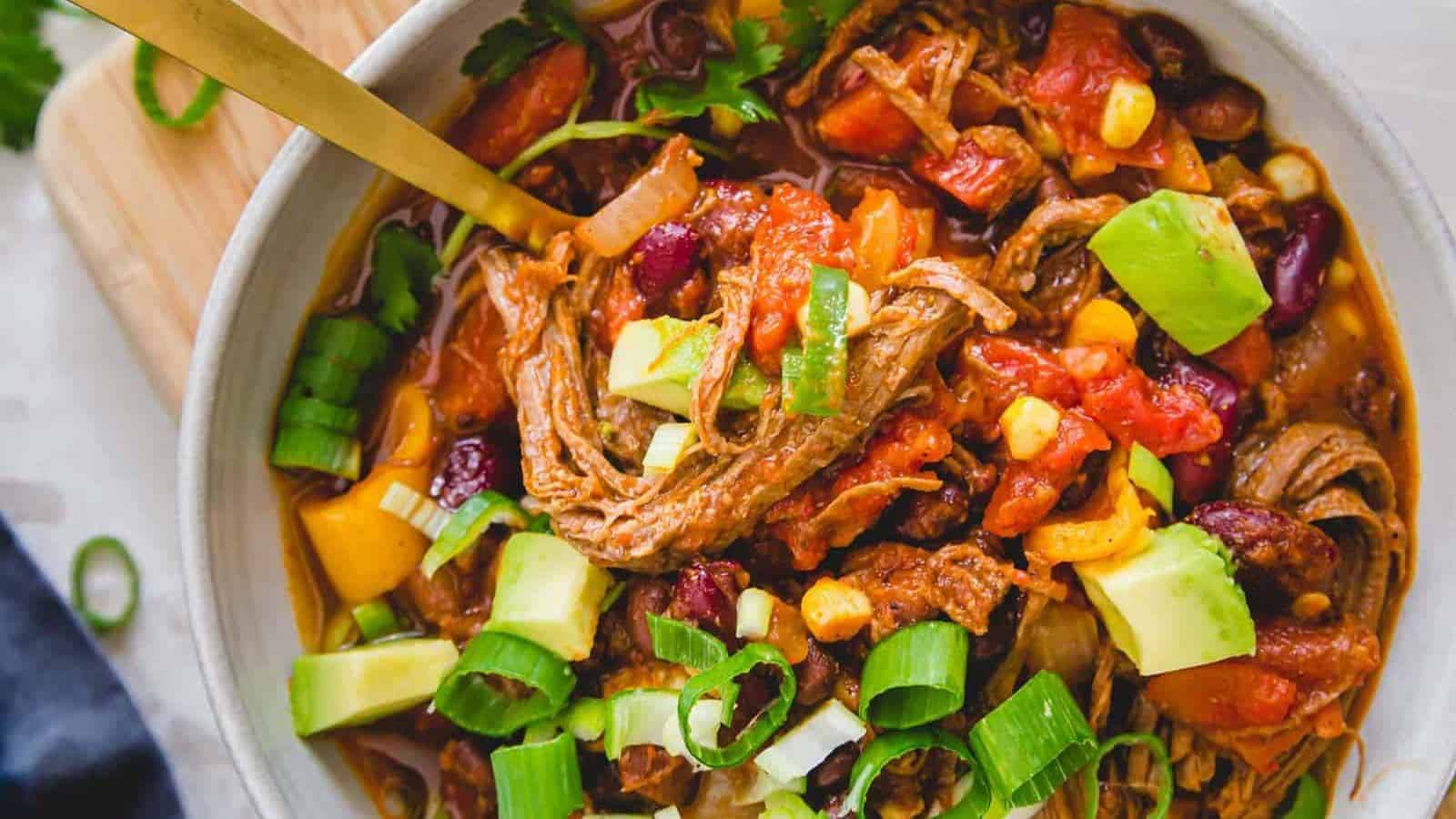 Brisket chili in a bowl topede with green onions and avocado.
