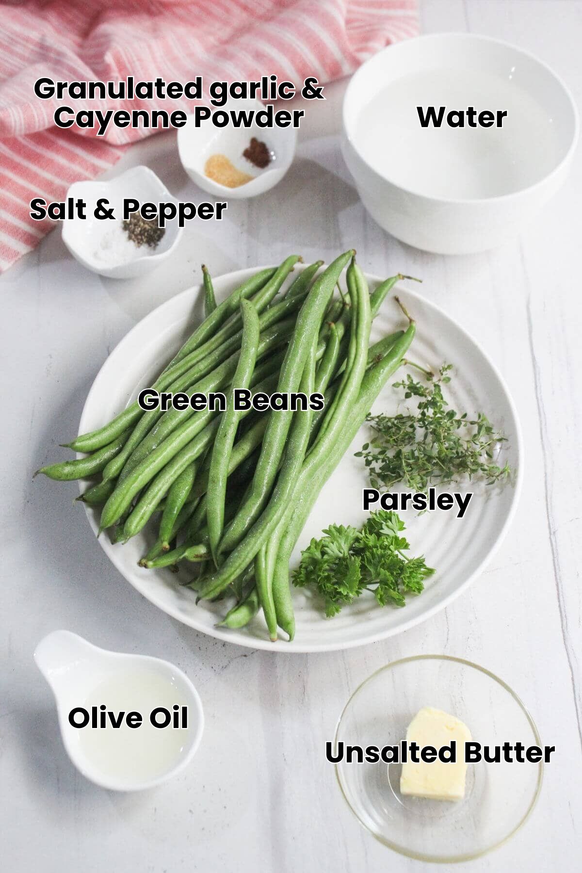 A white plate with fresh green beans, thyme, and parsley, surrounded by small bowls containing butter, oil, spices, and water, on a white surface.