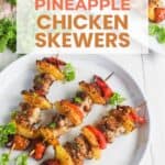 Two grilled chicken skewers with pineapple and red bell peppers are served on a white plate, garnished with parsley. Text overlay reads "Air Fryer Pineapple Chicken Skewers.
