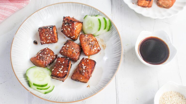 Plate with grilled tofu cubes topped with sesame seeds, cucumber slices on the side, and a small dish of soy sauce nearby.