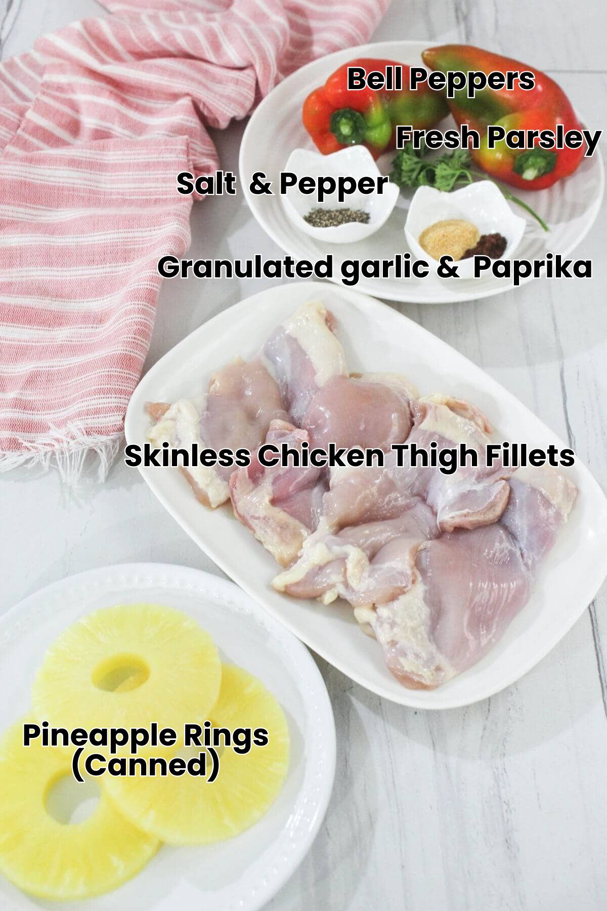 Raw chicken thighs on a plate, sliced pineapple rings, two whole bell peppers, small bowls of spices, and a pink striped cloth on a white surface.