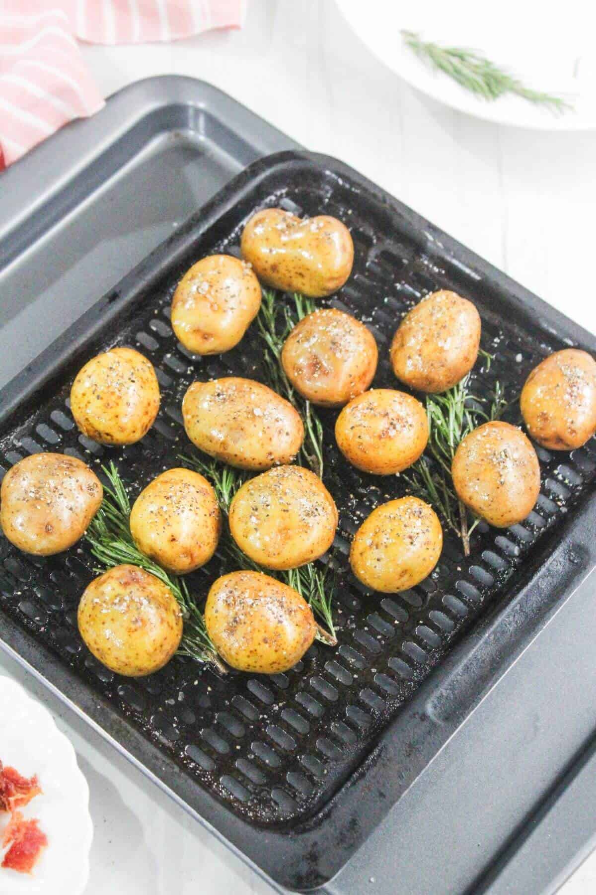 Tray of small roasted potatoes seasoned with pepper, arranged on a baking rack with sprigs of rosemary underneath.