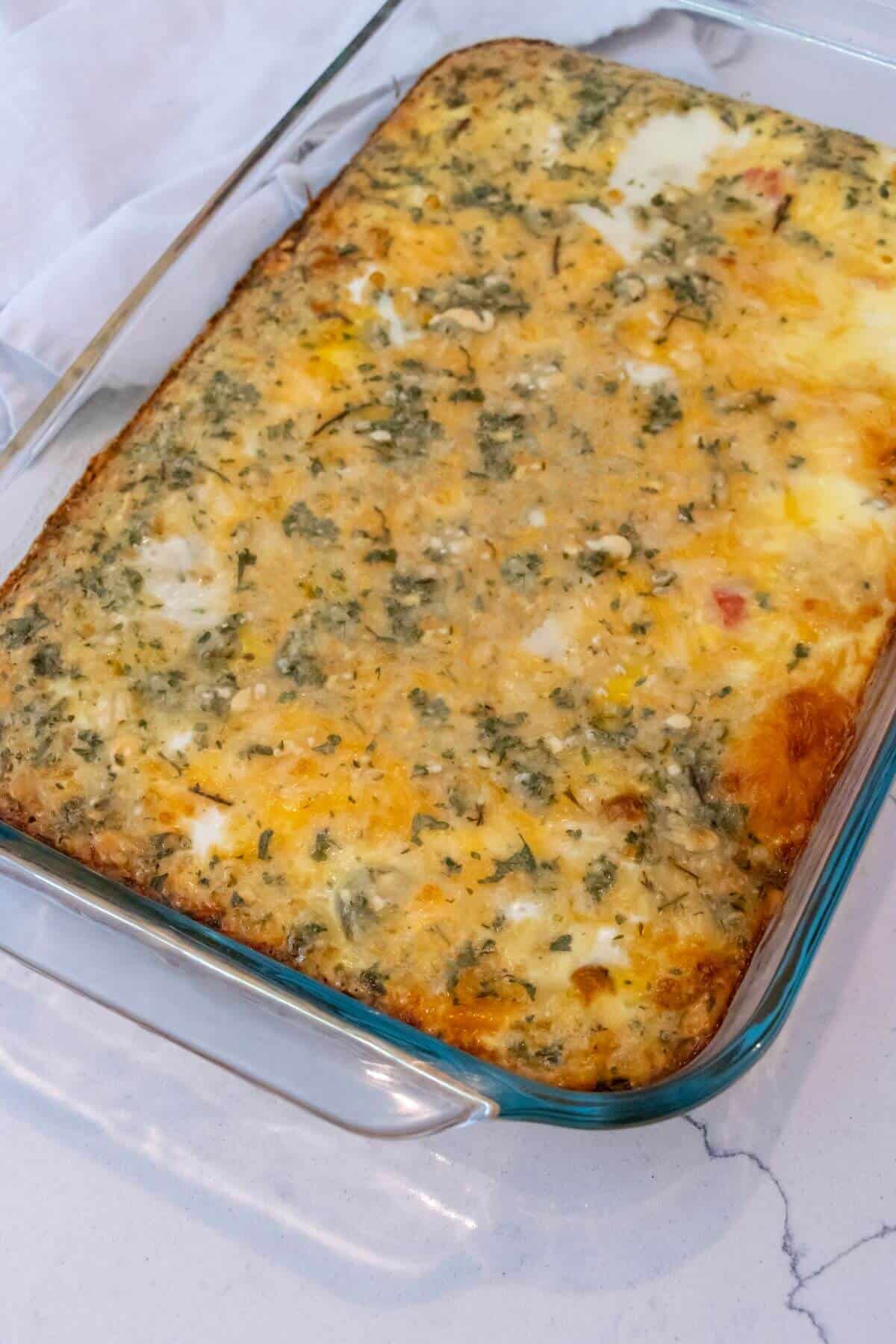 A baked egg casserole with herbs and cheese in a rectangular glass dish on a light countertop.
